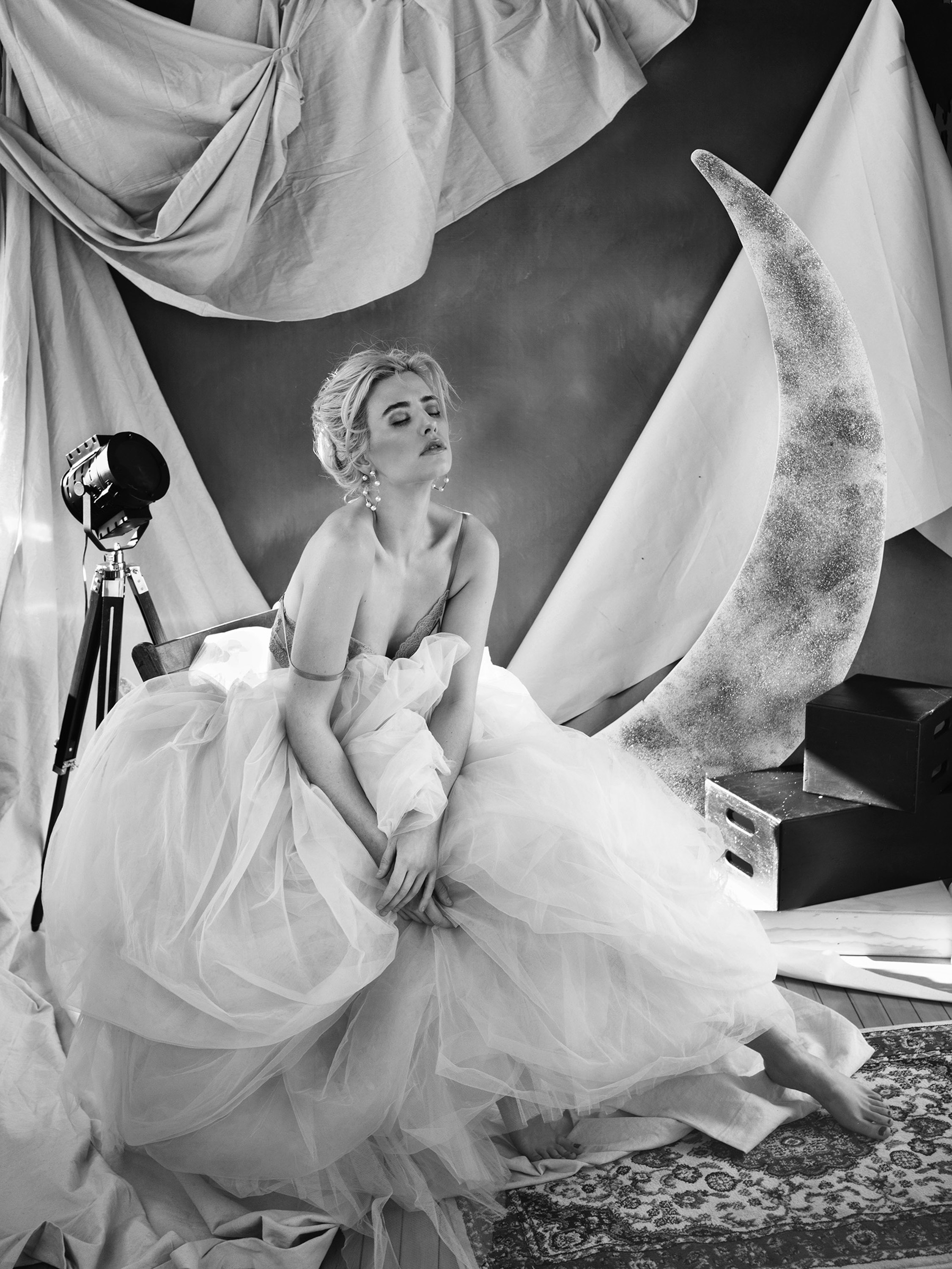 Dawn Muensterman in a white tulle gown seated on a crescent moon set, black and white